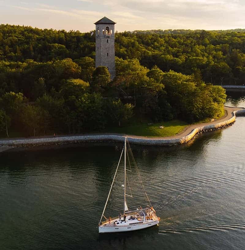 Rocky point lighthouse and sailboat on scenic harbor in Atlantic Coast, New England, showcasing coastal landscapes and maritime activities.