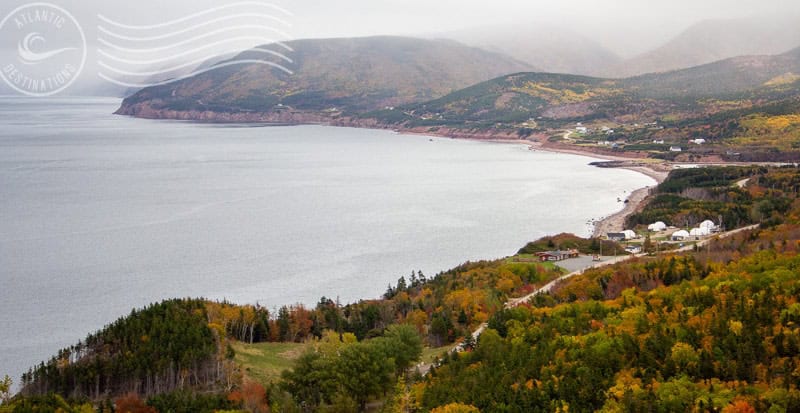 Serene coastal landscape with lush autumn foliage, rolling hills, and a tranquil waterfront, showcasing scenic destinations in Atlantic Canada during fall.