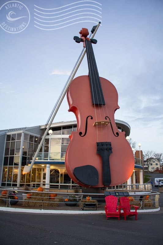 Violin sculpture outside Atlantic Destinations building, artistic musical landmark, large-scale violin display in coastal town, travel and tourism attraction, vibrant outdoor public art installation.