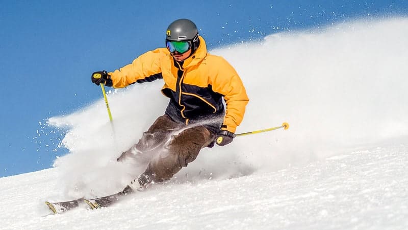 Things to do in North Carolina in winter-Vibrant skier in orange jacket carving through fresh mountain snow during winter sports adventure.