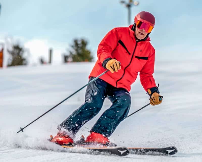 Skiing enthusiast wearing red jacket and goggles carving down snowy mountain slope during daytime.